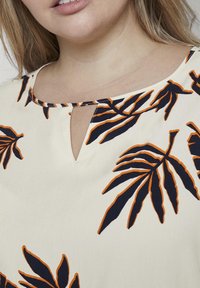 Blusa crema con scollatura a chiave, motivi fogliare in blu navy e arancione, e maniche corte. Una leggera texture aggiunge interesse visivo.