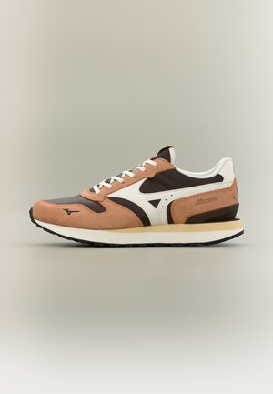 Καφέ, μαύρο και λευκό παπούτσι Mizuno με πάνελ από σουέτ και διχτυωτό υλικό, λευκά κορδόνια και μπεζ σόλα σε απλό μπεζ φόντο.