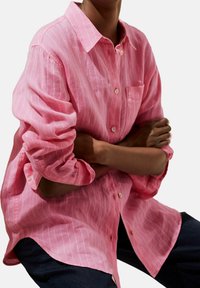 Camicia button-up a strisce rosa realizzata in tessuto leggero, con colletto, maniche lunghe e taschino sul petto. Fondo testurizzato, vestibilità rilassata.