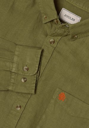 Chemise en lin vert olive à boutons, col boutonné, poche avant avec petit logo orange brodé, et étiquette Joules de marque à l'intérieur du col.