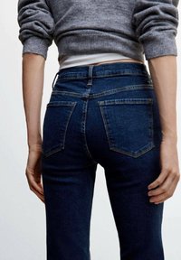 Jeans de mezclilla de un azul oscuro con un corte ajustado, que presentan dos bolsillos traseros, costuras sutiles y una cintura de tiro medio. Textura suave y diseño clásico.