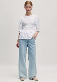 Witte peplumtop met een frons op de taille, gecombineerd met lichtblauwe wijde jeans. De top heeft korte mouwen en een ronde halslijn. Gladde stof.
