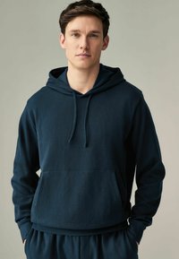 Sudadera con capucha de color azul marino, fabricada en un tejido suave, con un bolsillo canguro, capucha ajustable con cordón y puños acanalados.