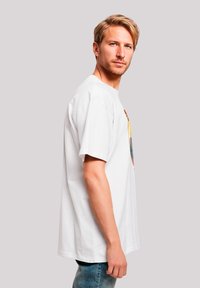 Weißes Baumwoll-T-Shirt mit einem bunten Grafikdruck auf der Vorderseite. Das Shirt hat einen lockeren Schnitt und kurze Ärmel. Hellblaue Jeans aus Denim.