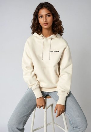 Felpa beige chiaro con tasca frontale e coulisse, con la scritta "C'est la vie" in nero sul petto. Abbinata a jeans azzurri chiari.