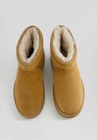 Brown suede ankle boots with faux fur lining, rounded top, and rubber sole, featuring stitching detail and a smooth texture.