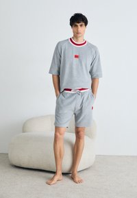 Grauer kurzärmeliger Sweatshirt mit rotem Akzentkragen und Logo-Patch, kombiniert mit passenden grauen Shorts mit elastischem Bund und roten Details.