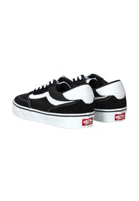 Sneaker basse in bianco e nero realizzate in suede e tela, con un design classico, lacci bianchi, cuciture e un logo Vans rosso.
