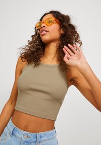 Top scurt ribbed de culoare verde măsliniu cu decolteu rotund, asociat cu blugi deschis la culoare, cu talie înaltă. Modelul poartă ochelari de soare mari, transparenți, de culoare galbenă.