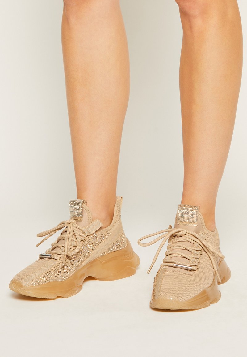 Beige atletik sko med mesh-overdel, prydet med rhinsten, gummisål og stofsnørebånd. Ankellang design med polstret krave.
