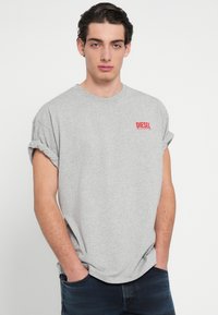 Sivá bavlnená tričko s vyhrnutými rukávmi. Na ľavej strane na hrudníku je červené logo „DIESEL“. Voľný strih so zaobleným výstrihom.