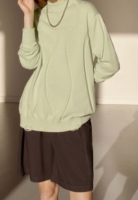 Ljusgrön stickad tröja med en texturerad design, försedd med hög krage och ribbade manschetter, kombinerad med en mörkbrun, lös passformkjol.