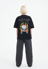 Svart överstor t-shirt med en färgglad dödskalle och låga grafik på baksidan. Har "Ed Hardy" text i silver, i kombination med lösa mörkgrå jeans.