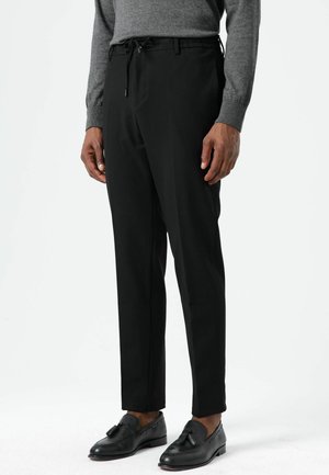 Pantalon noir effilé avec une taille à cordon de serrage. Tissu lisse avec une texture subtile. Assorti à des mocassins en cuir noir.