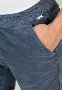 Pantalones cortos de pana en azul marino con una superficie texturizada, cinturilla elástica y bolsillos laterales. Presenta una pequeña etiqueta de la marca en la cinturilla.