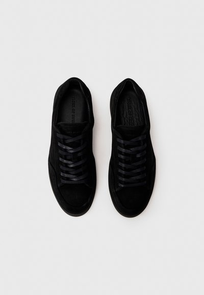 Sorte ruskind sneakers med flade snørebånd, rund tå, polstret krave og tekstureret indersål. Glat overflade uden mønstre eller synligt hardware.
