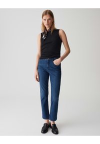 Top noir sans manches, jean en denim bleu et mocassins noirs. Le jean a une coupe droite avec une taille mi-haute et un design classique à cinq poches.