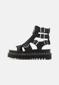 Sandali platform neri in pelle con più cinturini regolabili, fibbie metalliche e suola in gomma texturizzata con un dettaglio di cucitura gialla.