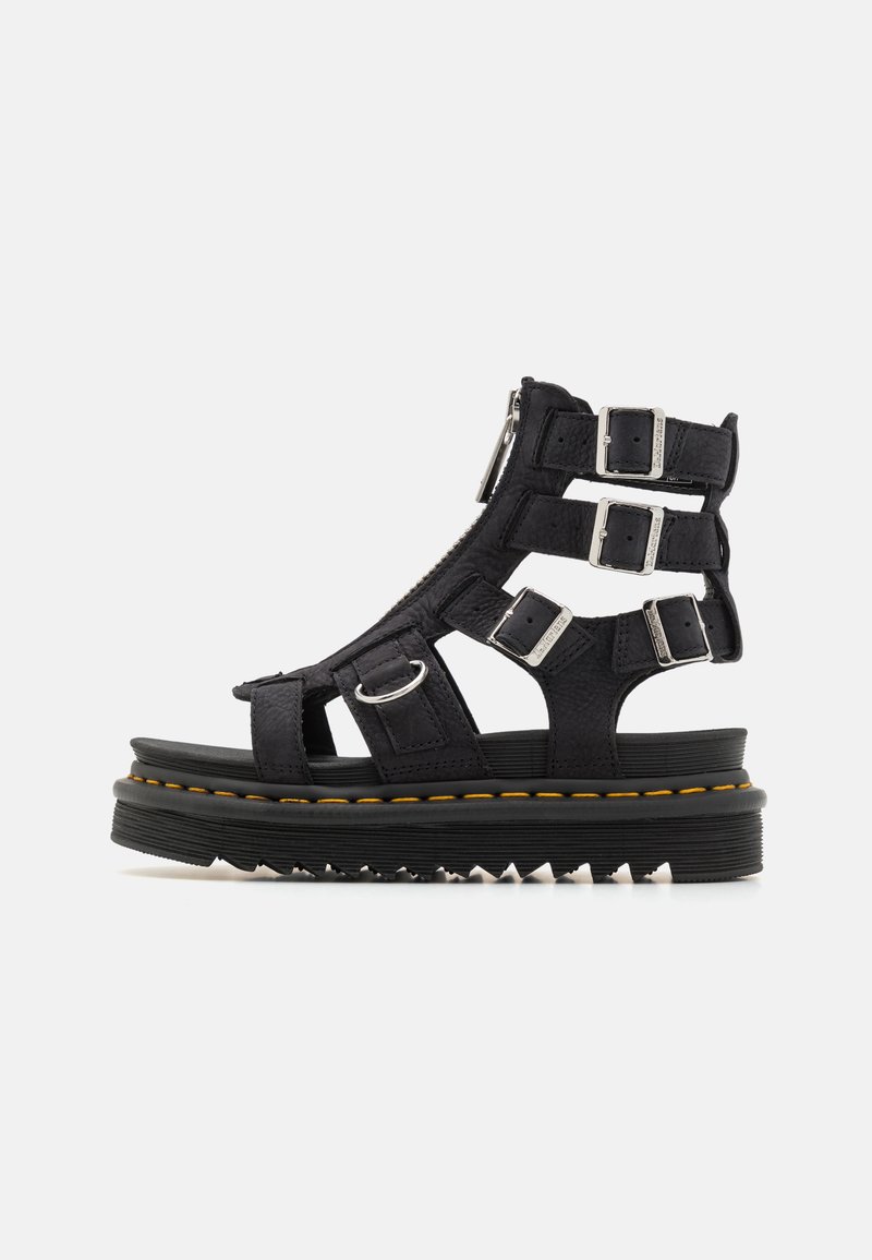 Sandalias de plataforma de cuero negro con múltiples correas ajustables, hebillas metálicas y una suela de goma texturizada con un detalle de costura amarilla.