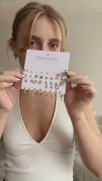 Σετ σκουλαρικιών χρυσού τόνου τοποθετημένο σε άσπρη κάρτα, με διάφορα σχέδια που περιλαμβάνουν καρφιά, κρουνωτές και πέρλες. Κείμενο: "ANNA FIELD."