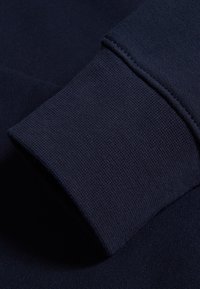 Puño de sudadera azul marino con un acabado texturizado y acanalado, con costuras visibles, que presenta un color sólido y una tela densa.