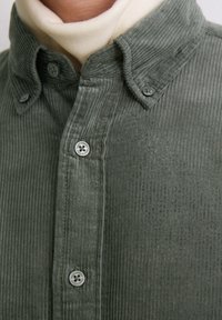Grünes Cordhemd mit Button-Down-Kragen, strukturiertem Stoff und zwei Knopfverschlüssen, das vertikale Rippdetails hervorhebt.