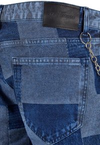 Traperice s patchwork dizajnom u različitim nijansama plave boje, s kožnom etiketom, detaljima na stražnjem džepu i lancem kao ukrasom.