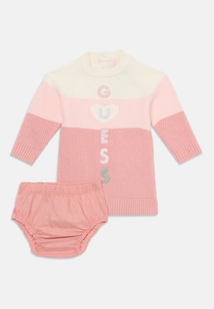 Ensemble de pull en maille de couleur rose clair et crème, comportant "GUESS" en lettres colorées et un short bloomer assorti en matière douce.