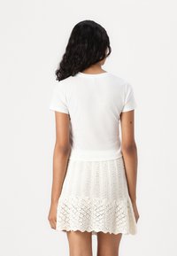 Camiseta blanca ajustada de manga corta, combinada con una falda de punto color crema que presenta un patrón de puntos abiertos y un dobladillo con forma de concha.