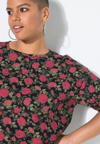 Czarny top w kwiaty z dużymi różowymi różami i zielonymi liśćmi, krótkie rękawy i okrągły dekolt. Lekka tkanina o gładkiej fakturze.
