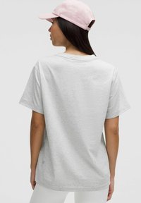 T-shirt en coton gris clair à manches courtes et col rond, porté avec une casquette rose, montrant une vue de dos simple et un design minimal.