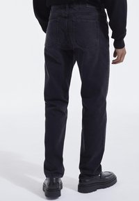 Jeans de mezclilla negra con corte recto, con dos bolsillos traseros y detalles de costura. Combinados con mocasines negros, que muestran una textura suave.