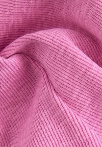 Rosa stof med en ribbet tekstur, der viser bløde, fine fibre og folder, som fremhæver en glat, let fuzzy overflade.