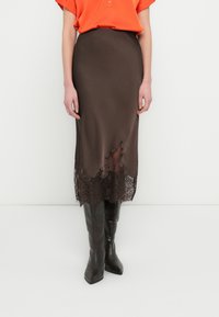 Brown satin skirt with a scalloped lace hem, complemented by a plain orange shirt and knee-high black boots. Smooth texture and fitted design.