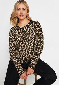 Maglione a maniche lunghe con stampa leopardata in tessuto a maglia beige, marrone e nero, con collo e polsini a costine, abbinato a pantaloni neri.