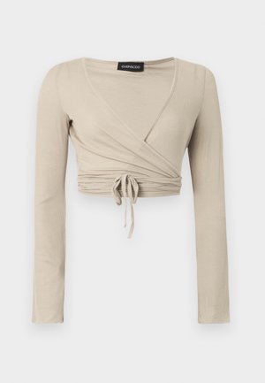 Bēšs, garām piedurknēm apņemošs tops ar V veida kakla izgriezumu un regulējamu sasiešanas lentīti viduklī. Izgatavots no ribota auduma ar piegulošu siluetu.