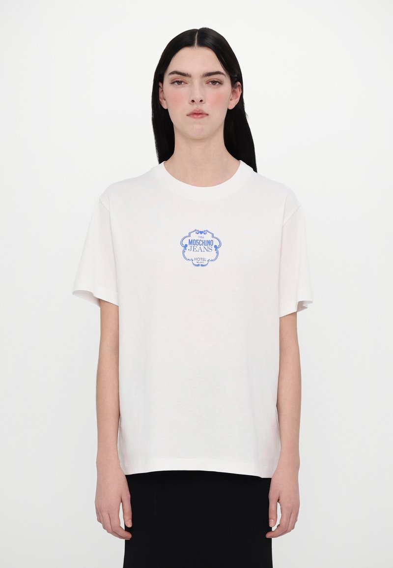 T-shirt de algodão branco com uma estampa gráfica azul que diz "MOSCHINO JEANS HOTEL." A camiseta tem mangas curtas e um corte descontraído.