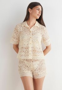 Kantenset met een korte mouwen knoopsluiting shirt en bijpassende shorts in crème, met bloempatronen en golvende randen. Zachte textuur.