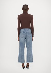 Maglietta marrone a maniche lunghe abbinata a jeans a vita alta larghi di colore blu chiaro, con orlo grezzo e tasche posteriori sottili. Sandali neri con tacco.