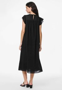 Juoda, vidutinio ilgio suknelė su trumpomis, volanėlėmis dekoruotomis rankovėmis ir detalėmis sprando srityje. Pagaminta iš lengvos medžiagos, turi laisvą siluetą.