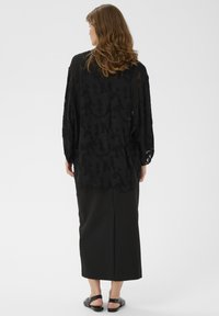 Juodas permatomas audinys su tekstūriniu gėlių raštu, laisvas kirpimas ir ilgos rankovės, derinamas su juoda ilga sijonu ir plokščiais sandalais.