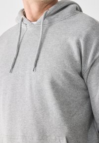 Felpa con cappuccio in cotone grigia dal taglio ampio, con cappuccio regolabile con coulisse, polsini a costine e tessuto morbido. Nessun motivo o dettaglio visibile.