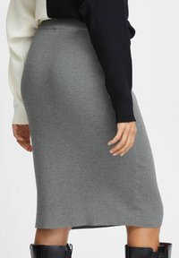 Gray ribbed pencil skirt with a fitted design, made from soft fabric. Features a high waist and a raw hem. Paired with a black top and boots.