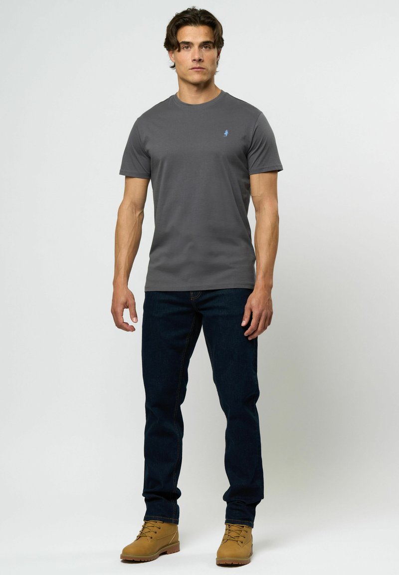 Grå t-skjorte med korte ermer og rund hals, kombinert med mørkeblå jeans og brune snøresko. Diskret logo på brystet.