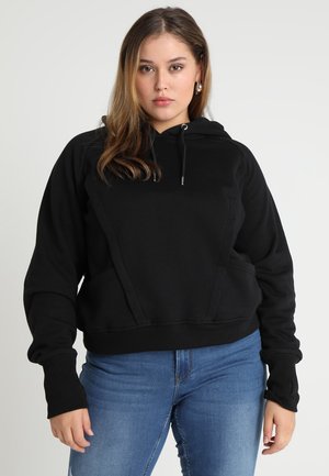 Sort hættetrøje med en struktureret overflade, kængurulomme og snoretræk i hætten. Har ribbede manchetter og kant. Bæres med blå denimbukser.