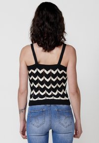 Canotta nera e crema lavorata a maglia con motivo a zigzag, con spalline larghe e fondo aderente. Abbinata a jeans in denim blu.