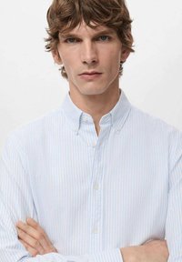 Camisa de botones a rayas azul claro y blanca con cuello, con una textura suave y detalles visibles de los botones en la parte delantera.