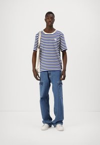 Camisa de manga corta a rayas azul y blanca, con cuello redondo, combinada con unos vaqueros cargo de corte holgado en un azul claro y zapatillas blancas.