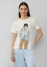 T-shirt en coton blanc avec une illustration colorée d'une personne portant une chemise à boutons bleu clair et un pantalon beige. Manches courtes, col rond.