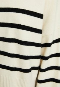 Gestrickter Pullover mit cremefarbenem Grundton und kräftigen schwarzen Streifen, ausgestattet mit einem gerippten Saum und weicher Textur. Fokus auf das horizontale Linienmuster.